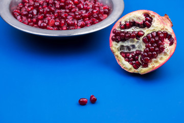 Pomegranate grains in a metal plate and half ripe pomegranate on a blue background