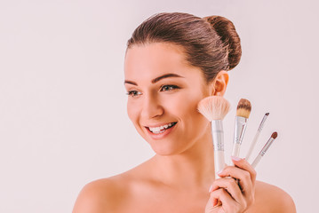 Portrait of young attractive woman model holding set of makeup brushes in hands and smiling. Attractive happy girl posing with make up visage fashion kit isolated. Makeup artist, stylish makeover