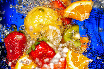Naklejka na ściany i meble Slices of fruits in water splash on dark blue background top view