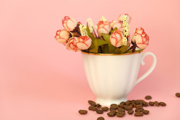 Porcelain cup with flowers and coffee beans on pink background. Good morning concept.