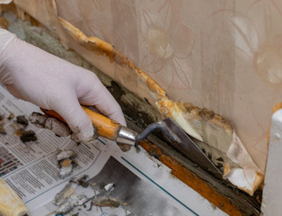 A gloved hand is spreading cement on a wall with a trowel. Construction works. Home repair. Do it...