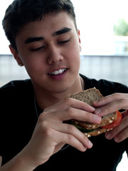 junger Mann isst ein Vollkornhaferbrot mit Tomaten-Gurken-Sandwich