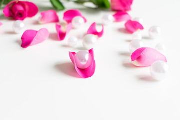 Pink, white, green flat lay: Pearls, pink rose petals, on white bright background. Beautiful set up. Top view, copy space, mock up. 