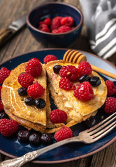 Sweet homemade pancakes with raspberries and blueberries on blue plate.