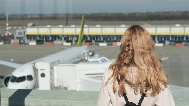 woman stands with her back and looks at the plane at the gate