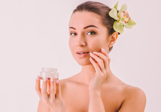 Attractive young woman applying face cream on cheek isolated. Beautiful sensual woman holding moisturizing lotion jar in hand isolated. Skincare cosmetics for clean skin. Beauty treatment routine