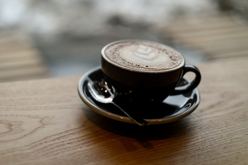 Coffee with latte art in a black cup on a wooden table inside a coffee shop