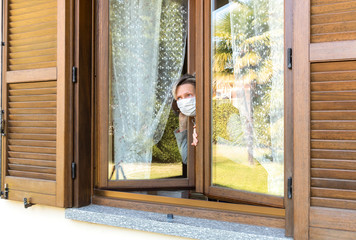 Woman wearing a protective medical face mask looking out from the window.
