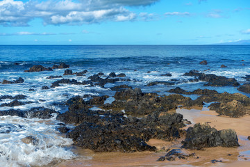 Black rocks on a beach in Maui, Hawaii, with view of blue ocean water.