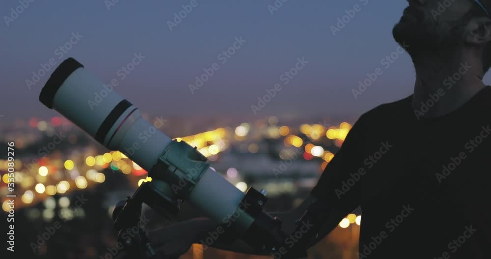 Wall mural astronomer with a telescope watching at the stars and moon with blurred city lights in the backgroun