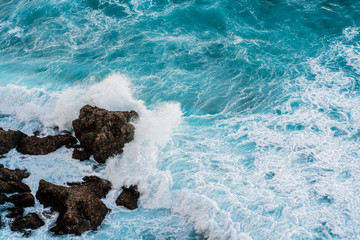 Powerful ocean waves break on the rocky shore. Aerial survey of the coastline of the island of Bali. Azure sea natural background.