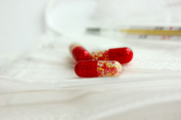 Medications are placed on white background at close distance. Red and white tablets without packaging. Thermometer shows high temperature. Background is blurred. Medicine chest. Mercury thermometer