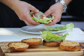 American cuisine. Fast food. Burgers with lettuce and sauce on a wooden board. Preparation with hands. Summer, picnic.  Background image, copy space