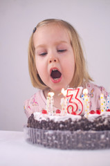 Little girl celebrate Happy Birthday with tasty cake and blows out the candles on the cake making a...