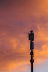 Cellular communications tower on beautiful dramatic clouds background in evening, vertical view.