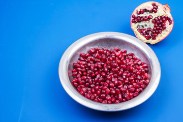 Pomegranate grains in a metal plate and half ripe pomegranate on a blue background