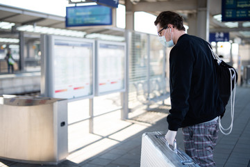 Mann mit Koffer auf dem Bahnsteig, er schützt sich mit Mundschutz und Handschuhen vor einer Ansteckung mit dem Coronavirus