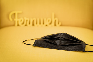 A black face mask on a yellow background with a sign in the background that stands for wanderlust, travel, adventure and vacation in times of the Covid-19 crisis, travel restrictions and isolation