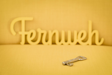 A simple key on a yellow background with a blurred sign in the background that stands for wanderlust, travel and adventure; concept, mood image 