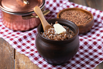 Traditional russian simple meal: cooked buckwheat porridge with brown butter in clay pot. Healthy food, low calories, easy to cook. Copper pan, wooden backround, close up