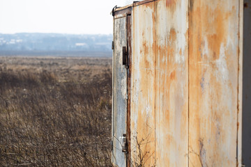 An iron old rusty garage stands in a field and pollutes nature.