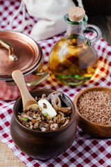 Traditional russian simple meal: cooked buckwheat porridge with fried mushrooms and vegetables in clay pot. Healthy food, easy to cook. Copper pan, wooden backround, home kitchen atmosphere close up