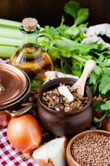 Traditional russian simple healthy meal: cooked buckwheat porridge with fried mushrooms, vegetables, butter in clay pot. Healthy food, low calories. Copper pan, wooden background, close up