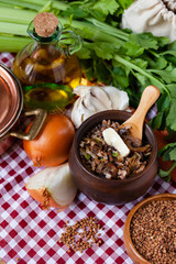 Traditional russian simple healthy meal: cooked buckwheat porridge with fried mushrooms, vegetables, butter in clay pot. Healthy food, low calories. Copper pan, wooden background, close up
