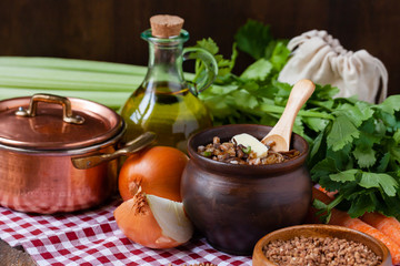 Traditional russian simple healthy meal: cooked buckwheat porridge with fried mushrooms, vegetables, butter in clay pot. Healthy food, low calories. Copper pan, wooden background, close up