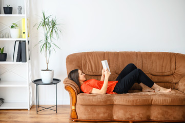 Woman lies on the sofa and reads a book