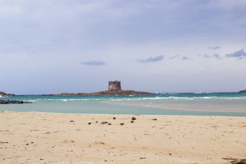 Amazing  view on the old aragonese tower in La Pelosa Beach. Beautifull beach with white sands, waves with foam and cloudly sky in Stintino, Sardinia, Italy