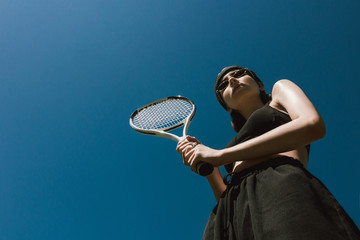 Girl on a tennis court Bottom view photo Girl in black sportswear is holding a tennis racket on...
