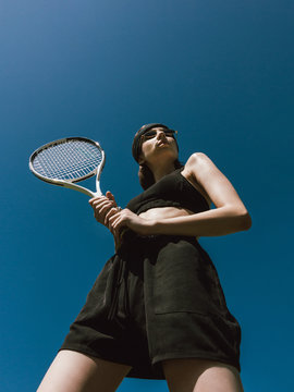 Tennis player Bottom view photo with copy space Girl in black sportswear is holding a tennis racket on blue sky background