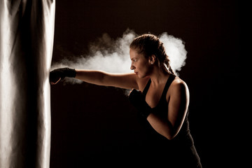kick fighter girl punching a boxing bag. smoke and dark background
