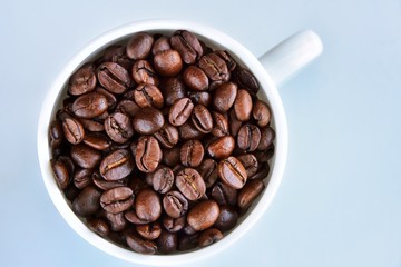 Roasted coffee beans in porcelain mug with selective focus on neutral background. Arabica coffee seeds in the coffee cup