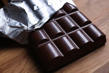 Close-up of dark chocolate bar in foil with open cover laying on wooden table. Unpacked sweets with nut. Calories and antioxidant. Sweet and yummy dessert concept - Powered by Adobe