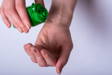 One hand holds a green open bottle of antiseptic. Disinfection liquid is poured from the bytka on the other hand. Personal hygiene, health and prevention. Remedy for bacteria, viruses, coronavirus