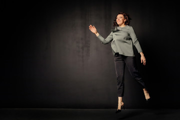 Successful business woman in a gray blouse jumps and rejoices on black background. Free space. Attractive businesswoman on a black background. Copy space