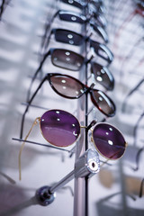 A row of glasses to protect from the sun. Store points. Stand with sunglasses in the optics store. Female hand shows glasses. Presentation of points. Close-up