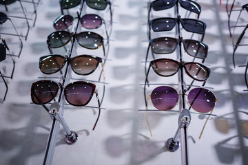 A row of glasses to protect from the sun. Store points. Stand with sunglasses in the optics store. Female hand shows glasses. Presentation of points. Close-up