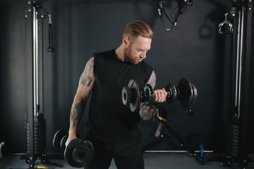 fitness trainer in dark clothes lifts dumbbells right in front of him