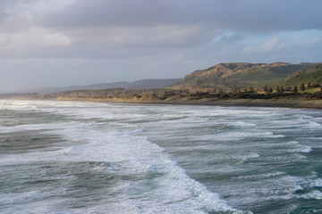 aerial landscape of sunset over Muriwai beach with waves in the foreground and a typical New Zealand coastal landscape