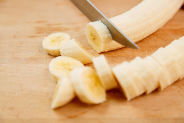 Female hand cuts banana with smoothie rings on a wooden board with a knife.