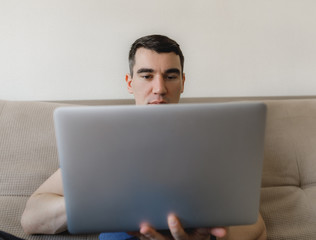 a young guy in a blue T-shirt is European sitting at home on the couch, working remotely and communicating with friends online on a notebook with a phone and a diary