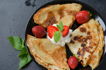 black plate with pancakes with strawberries and cream on a black background, top view