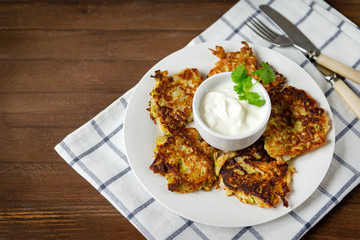 plate with zucchini pancakes with sour cream, towel on a wooden background, top view