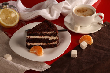 A piece of cake, a Cup of coffee and a lemon on a glossy red table