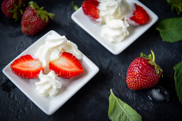 strawberries with whipped cream on a plate, mint leaves on a black background, fresh berries, close up, dessert