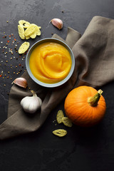 Butternut squash soup with croutons, garlic and spices in ceramic bowl on grunge black background with linen napkin. Top view