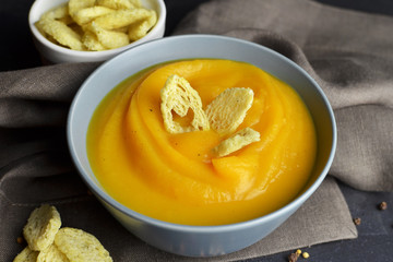 Pumpkin autumn soup with wheat croutons in ceramic bowl on dark linen background. Thanksgiving day meal